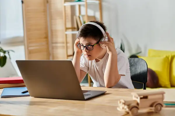 Little boy with Down syndrome wearing headphones uses laptop at home. — Stock Photo