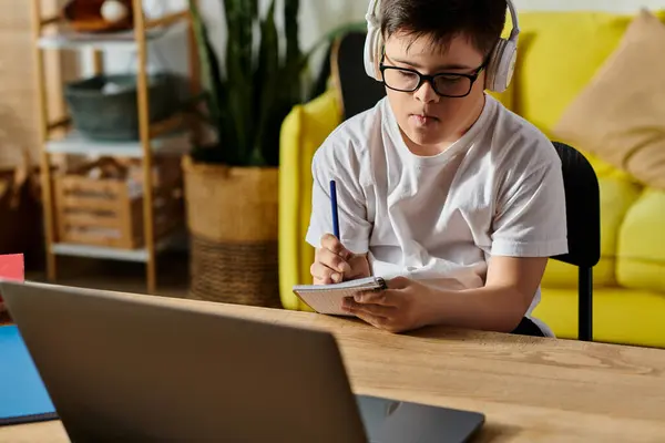 A adorable boy with Down syndrome is engrossed in using a laptop and wearing headphones at a table. — Stock Photo