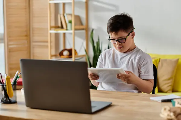 Adorabile ragazzo con sindrome di Down con occhiali immersi nelle attività del computer portatile a casa. — Foto stock