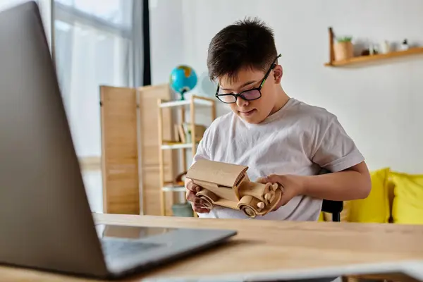 Un garçon trisomique s'assoit avec diligence à un bureau, se concentrant sur son ordinateur portable. — Photo de stock