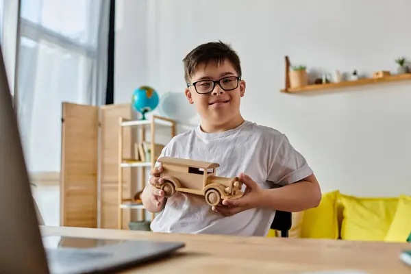 Adorable boy with Down syndrome playing with a wooden toy car in front of a laptop. — Stock Photo