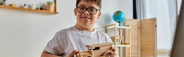 Мальчик с синдромом Дауна в очках играет с деревянной игрушечной машиной. — стоковое фото