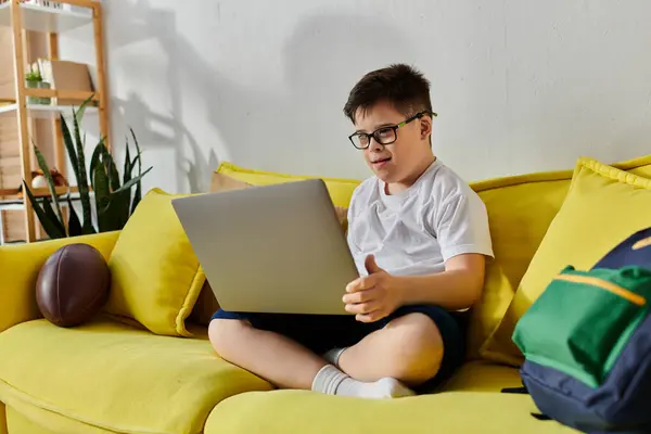 Little boy with Down syndrome using laptop on yellow couch. — Stock Photo