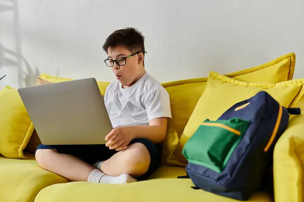 Cute boy with Down syndrome using laptop on yellow couch. — Stock Photo