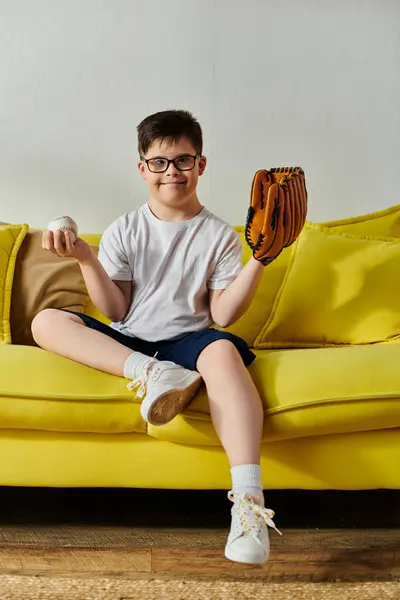 Menino adorável com síndrome de Down sentado no sofá com luva de beisebol. — Fotografia de Stock