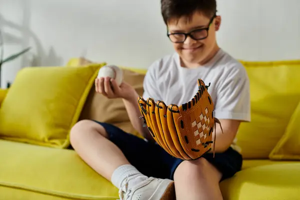 A boy with Down syndrome sits on a couch with a baseball glove. — Stock Photo
