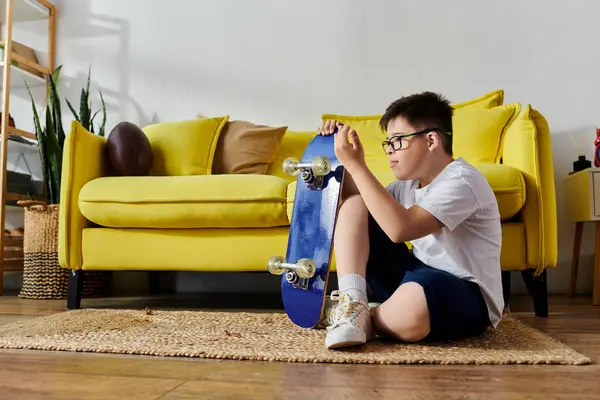 Adorable boy with Down syndrome happily sitting on the floor with a skateboard in his room. — Stock Photo