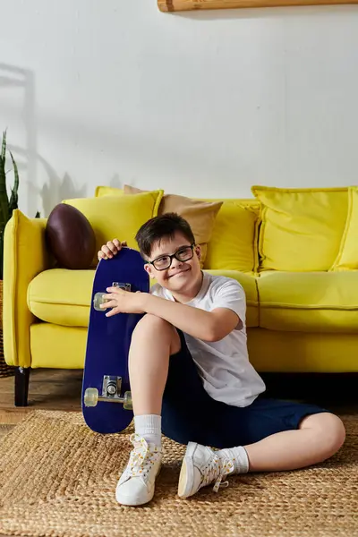 Adorable boy with Down syndrome holds skateboard near yellow couch. — Stockfoto