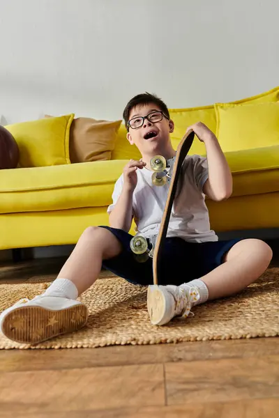 Ein entzückender Junge mit Down-Syndrom sitzt mit einem Skateboard auf dem Boden. — Stockfoto