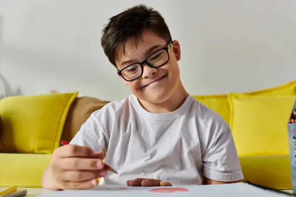 A adorable boy with Down syndrome with glasses drawing on a vibrant yellow couch. — Stock Photo