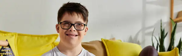 A adorable boy with Down syndrome with glasses sits calmly on a couch in a cozy room. — Stock Photo