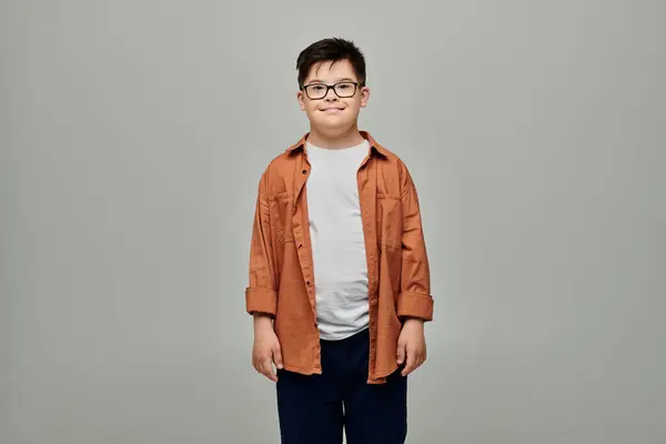Un niño encantador con síndrome de Down con gafas se levanta sobre un fondo gris. - foto de stock