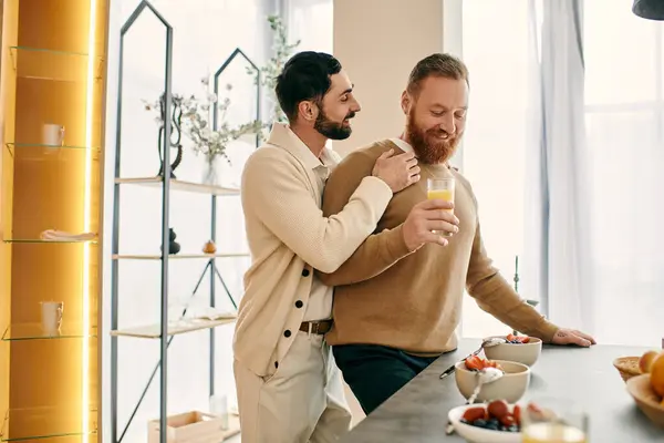 Two men enjoying a glass of orange juice in a cozy kitchen, sharing a moment of happiness and love in their modern apartment. — Stock Photo