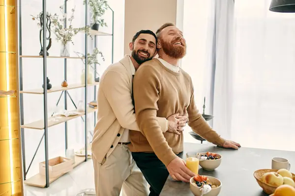 Two happy men, a gay couple, embrace in a warm hug in a modern kitchen, showcasing their love and bond. — Stock Photo