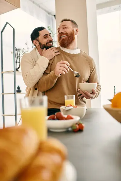 Dos hombres se abrazan en la cocina mientras disfrutan del desayuno juntos en un apartamento moderno, expresando su amor y afecto. - foto de stock