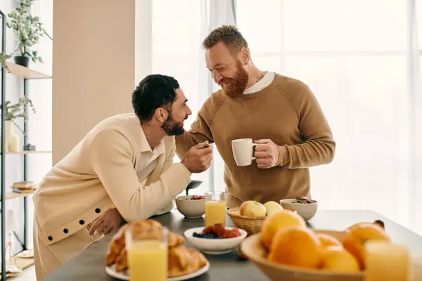 A happy gay couple sit together at a kitchen table, savoring a morning meal in their modern apartment. — Stock Photo
