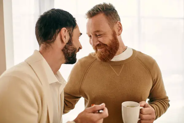 Due uomini, una coppia gay felice, che conversano con tazze di caffè in un appartamento moderno, mostrando il loro amore e legame. — Foto stock