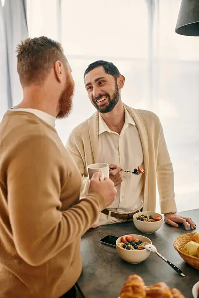 Deux hommes heureux, un couple gay aimant, savourant le petit déjeuner ensemble dans une cuisine moderne remplie de chaleur et d'amour. — Photo de stock