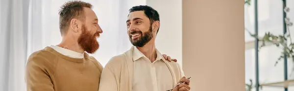 Deux hommes partagent un moment charmant, se souriant devant une fenêtre lumineuse dans un appartement moderne. — Photo de stock