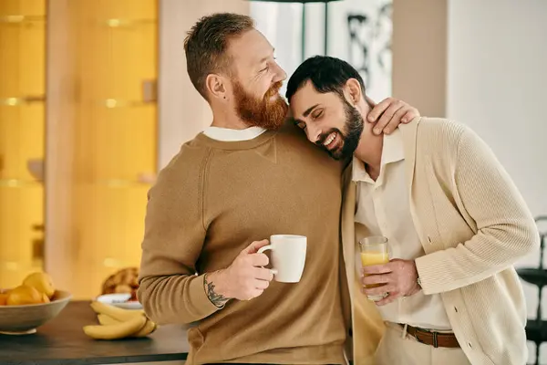 Two men, a happy gay couple, hug affectionately while savoring coffee in a modern kitchen, showcasing their love and connection. — Stock Photo