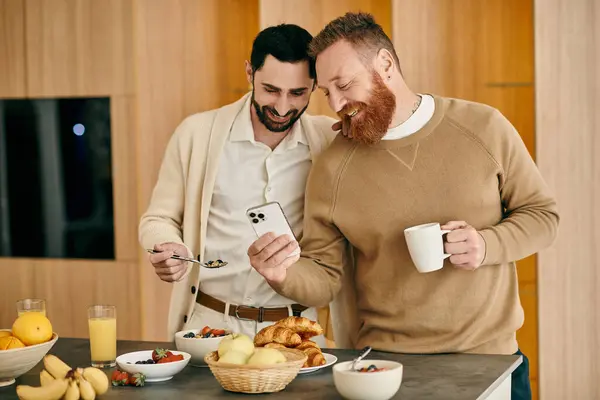 Two men enjoy breakfast in a stylish kitchen, absorbed in phone while sharing intimate moments. — Stock Photo