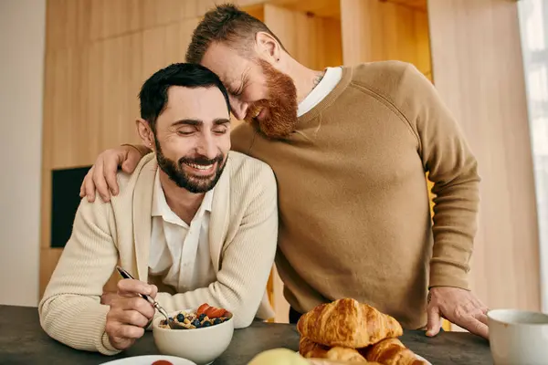 Двое мужчин с радостью делятся завтраком на стильной кухне, создавая вместе заветные воспоминания. — стоковое фото