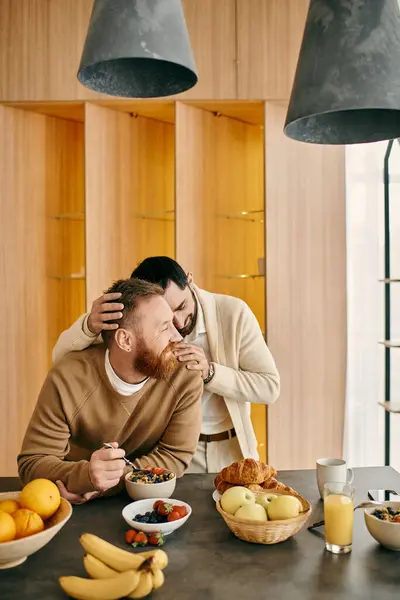 Um alegre casal gay desfrutando de café da manhã juntos em uma mesa em seu apartamento moderno. — Fotografia de Stock