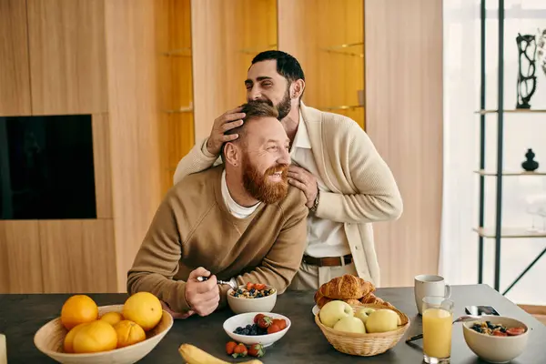 Двое мужчин, счастливая гей-пара, сидят за столом в современной квартире, наслаждаясь совместным завтраком. — стоковое фото