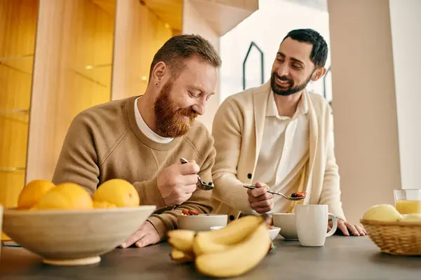 Dos hombres barbudos, una feliz pareja gay, compartiendo una comida en una cocina moderna. - foto de stock