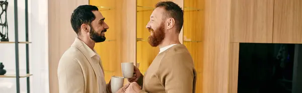 A happy gay couple standing closely together in a modern living room, enjoying quality time and showing affection. — Stock Photo