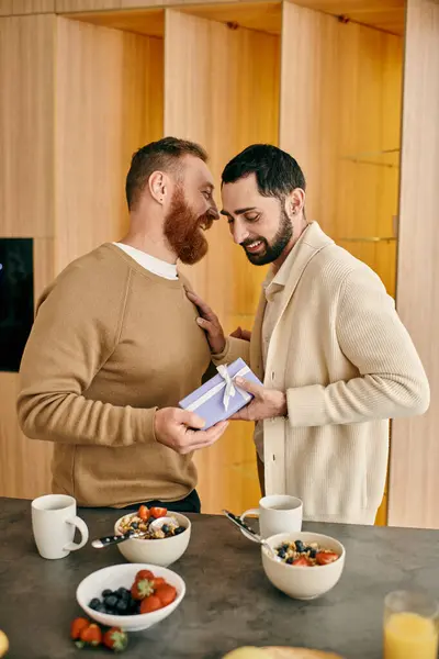 A man joyfully presents a gift to his partner in their modern kitchen, celebrating love and togetherness. — Stock Photo