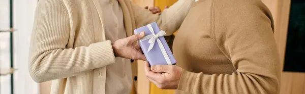 A man joyfully presents a gift to his partner in their modern apartment, expressing love and appreciation in a heartfelt moment. — Stock Photo
