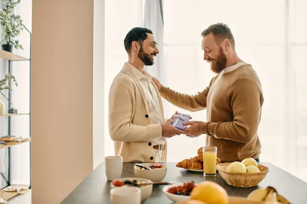 Two happy men exchange gift in a cozy kitchen, radiating love and joy as they share a special moment. — Stock Photo