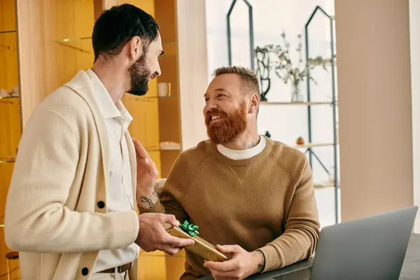 A man warmly presents a gift to another man in a store, their smiles reflecting the shared love and affection. — Stock Photo