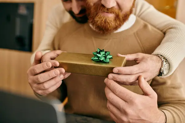 A man with a beard joyfully holds a gift box, expressing love and gratitude in a modern apartment. — Stock Photo