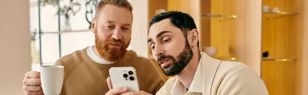 Um homem segurando uma xícara de café e outro homem segurando um telefone, desfrutando de um momento acolhedor juntos em um apartamento moderno. — Fotografia de Stock