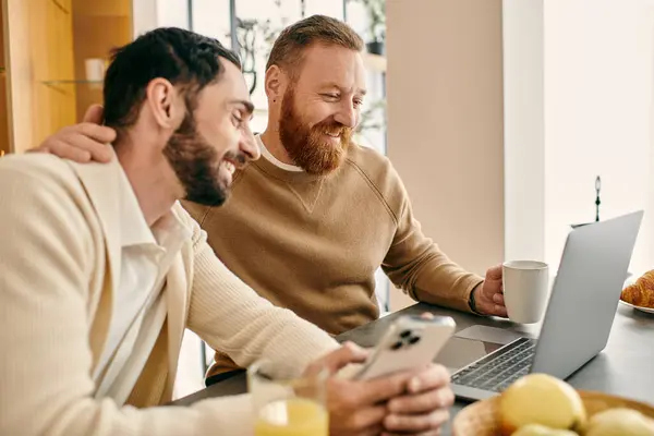 Two men engrossed in laptop content while seated at a table in a modern apartment, expressing togetherness and connection. — Stock Photo