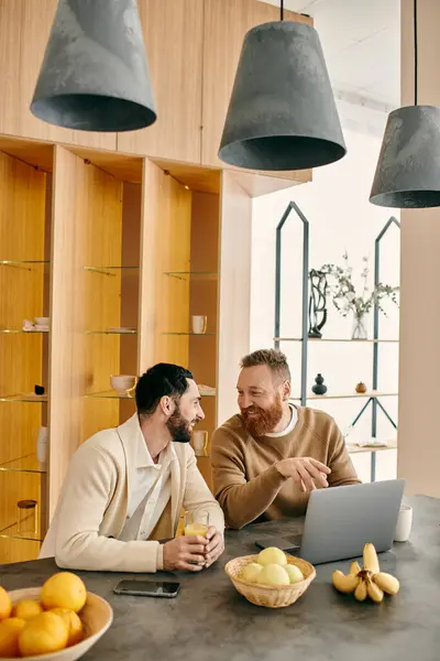 A happy gay couple sitting at a table in a modern kitchen, engrossed in conversation over coffee, enjoying each others company. — Stock Photo