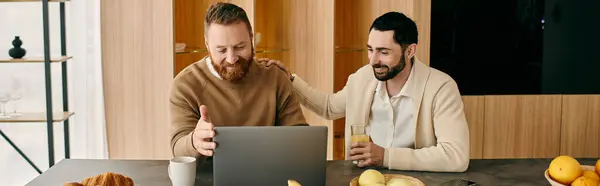 Two men sit at a table, engrossed in their laptop, collaborating and sharing ideas in a modern apartment setting. — Stock Photo