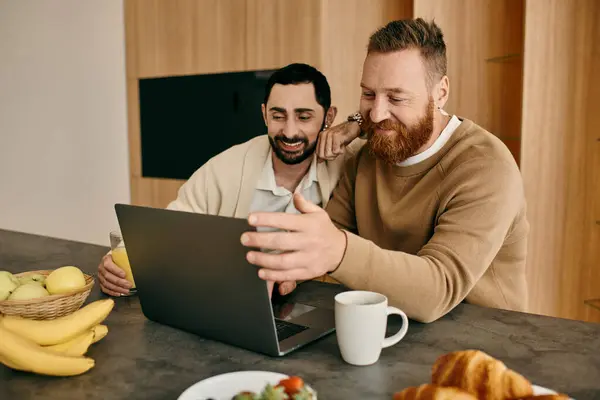 Two men immersed in work, sitting at a table and sharing a laptop in a cozy, modern apartment. — Stock Photo