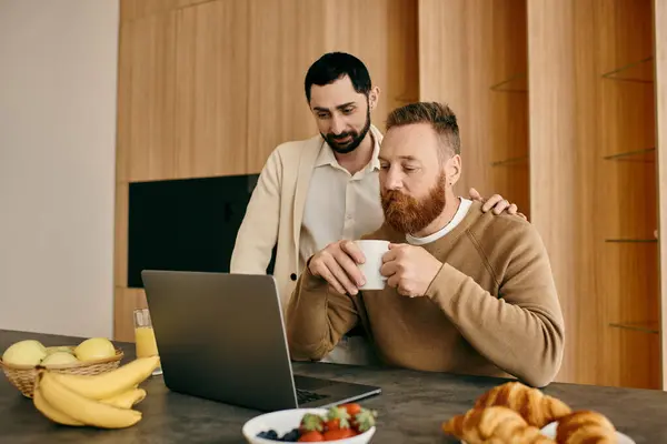 Two men, a happy gay couple, sit at a kitchen table, engrossed in a laptop screen, creating a bond of shared interest and love. — Stock Photo
