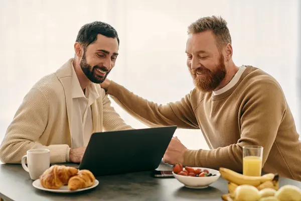 Two men immersed in a laptop screen at a table in a modern setting, engaged in a shared activity. — Stock Photo