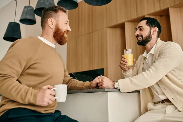 Dos hombres, una feliz pareja gay bebiendo jugo de naranja en una cocina moderna. - foto de stock