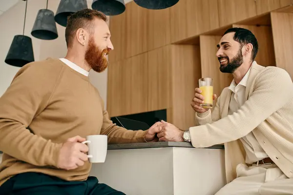 Dos hombres, una feliz pareja gay bebiendo jugo de naranja en una cocina moderna. - foto de stock