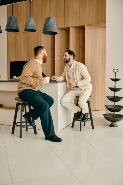 Una coppia gay felice seduta su sgabelli in una cucina moderna, godendosi reciprocamente compagnia e trascorrendo del tempo di qualità insieme. — Foto stock