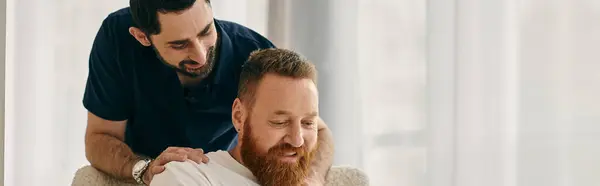 Casual gay couple in modern living room, one man with a beard sits on a couch next to his partner. — Stock Photo