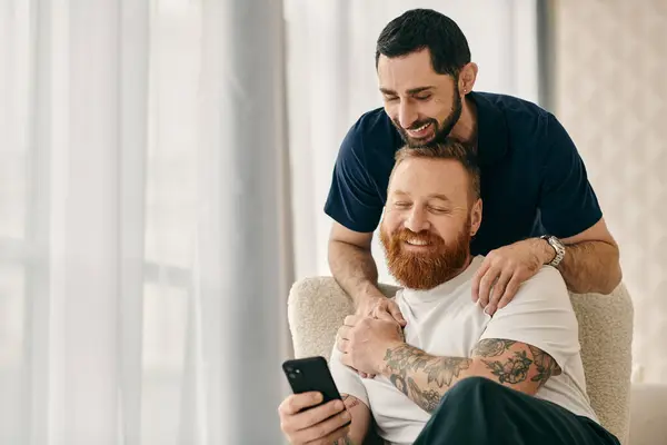 Two men in casual clothes sit on a couch, engrossed in a cell phone together in a modern living room. — Stock Photo