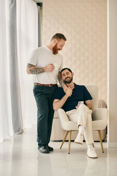 Two men, a happy gay couple, sit closely on a chair in a modern living room, enjoying quality time together. — Stock Photo