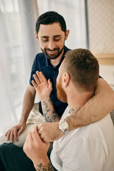 Two men with arm tattoos sitting on a bed, enjoying each others company in a modern living room. — Stock Photo