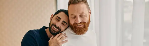 Two men in casual attire hug affectionately in front of a large window, embodying love and togetherness. — Stock Photo